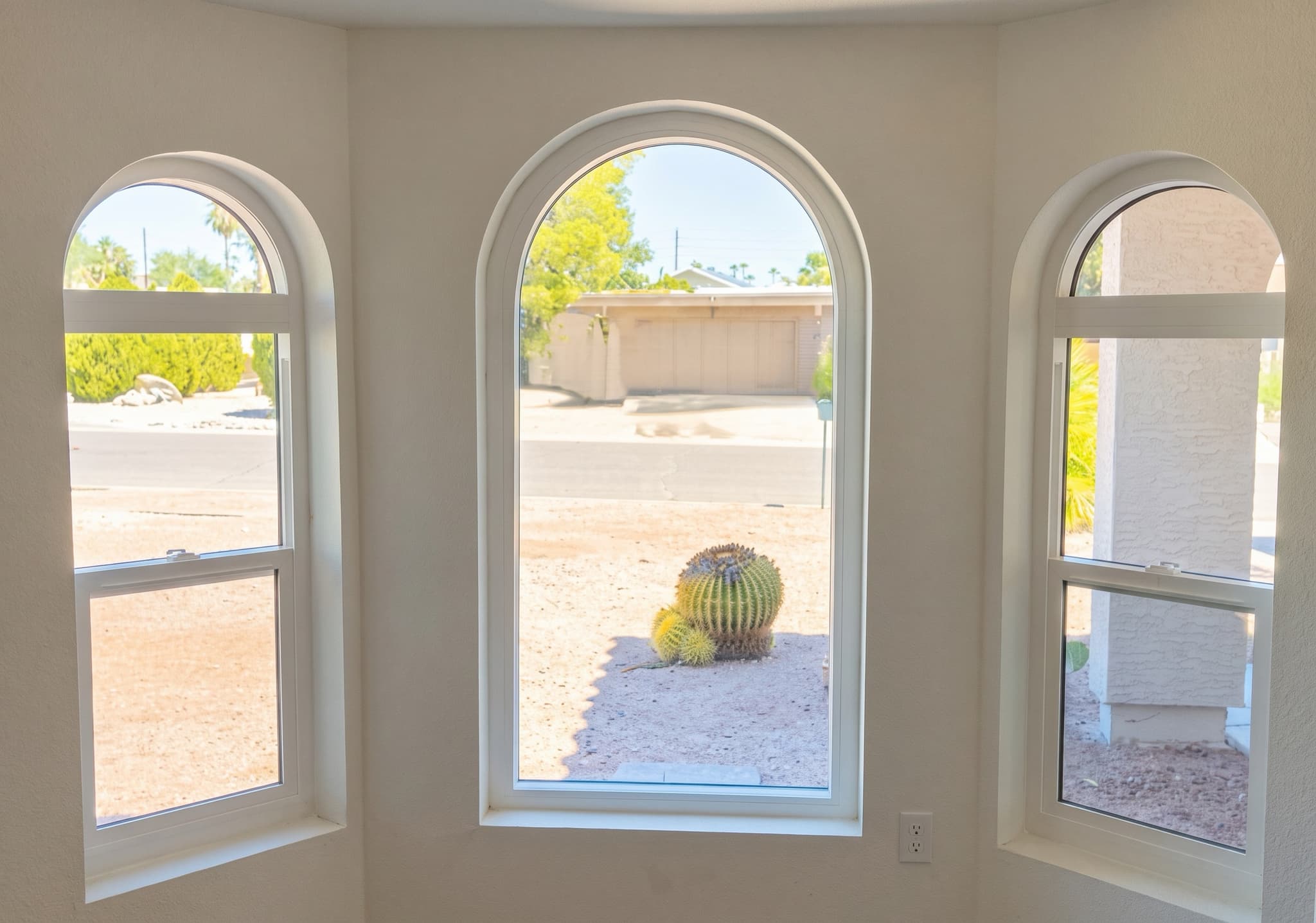Three arched-top windows in a bay, looking out to desert landscaping