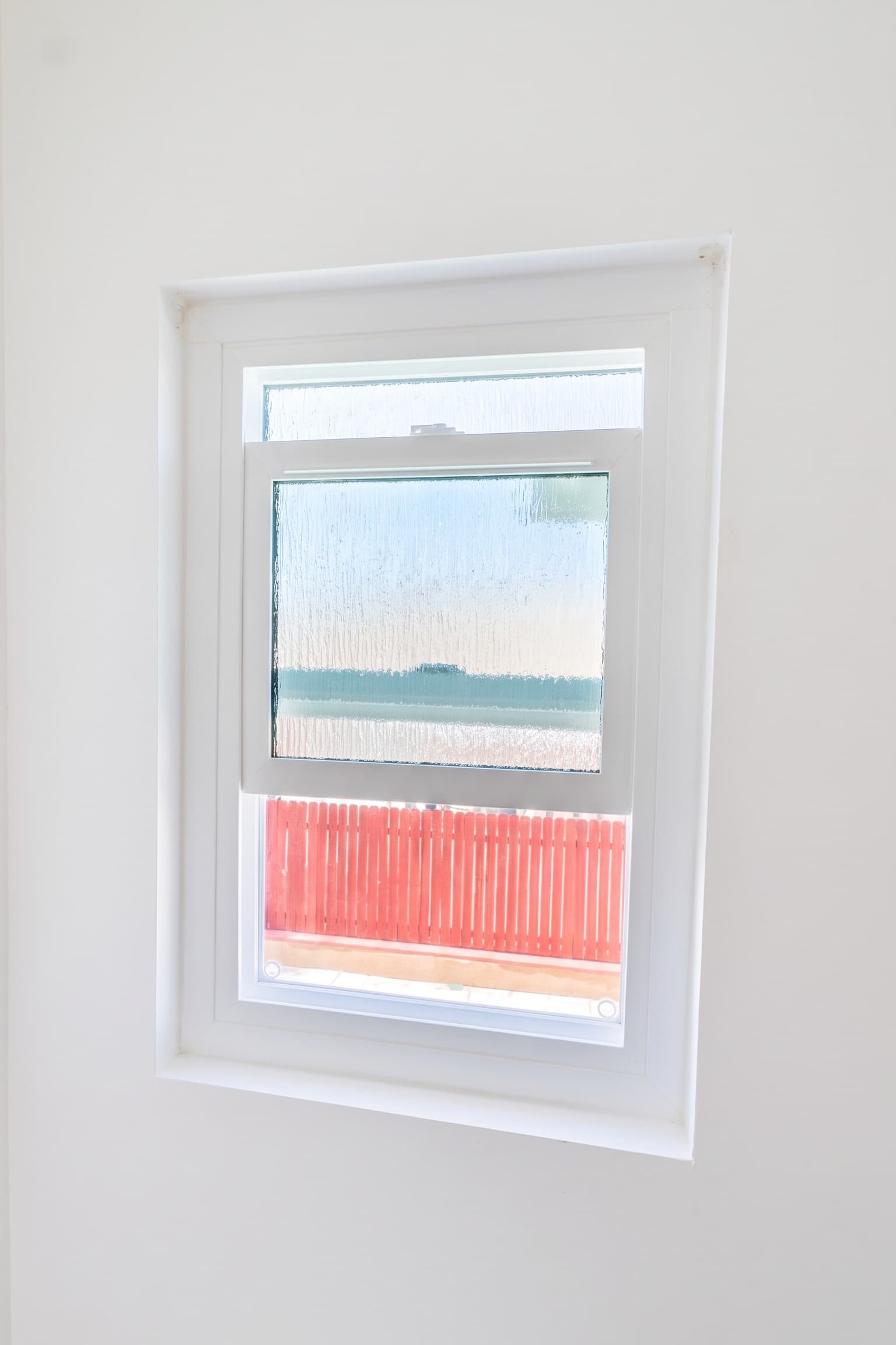 Single-hung bathroom window with rain-textured privacy glass, lower sash raised