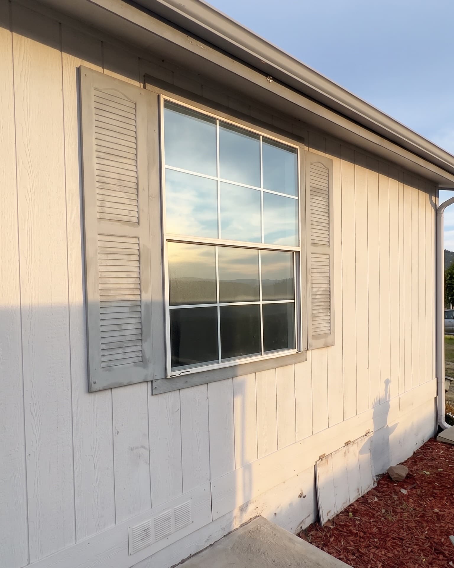 White window with colonial grids and grey shutters on a sided home