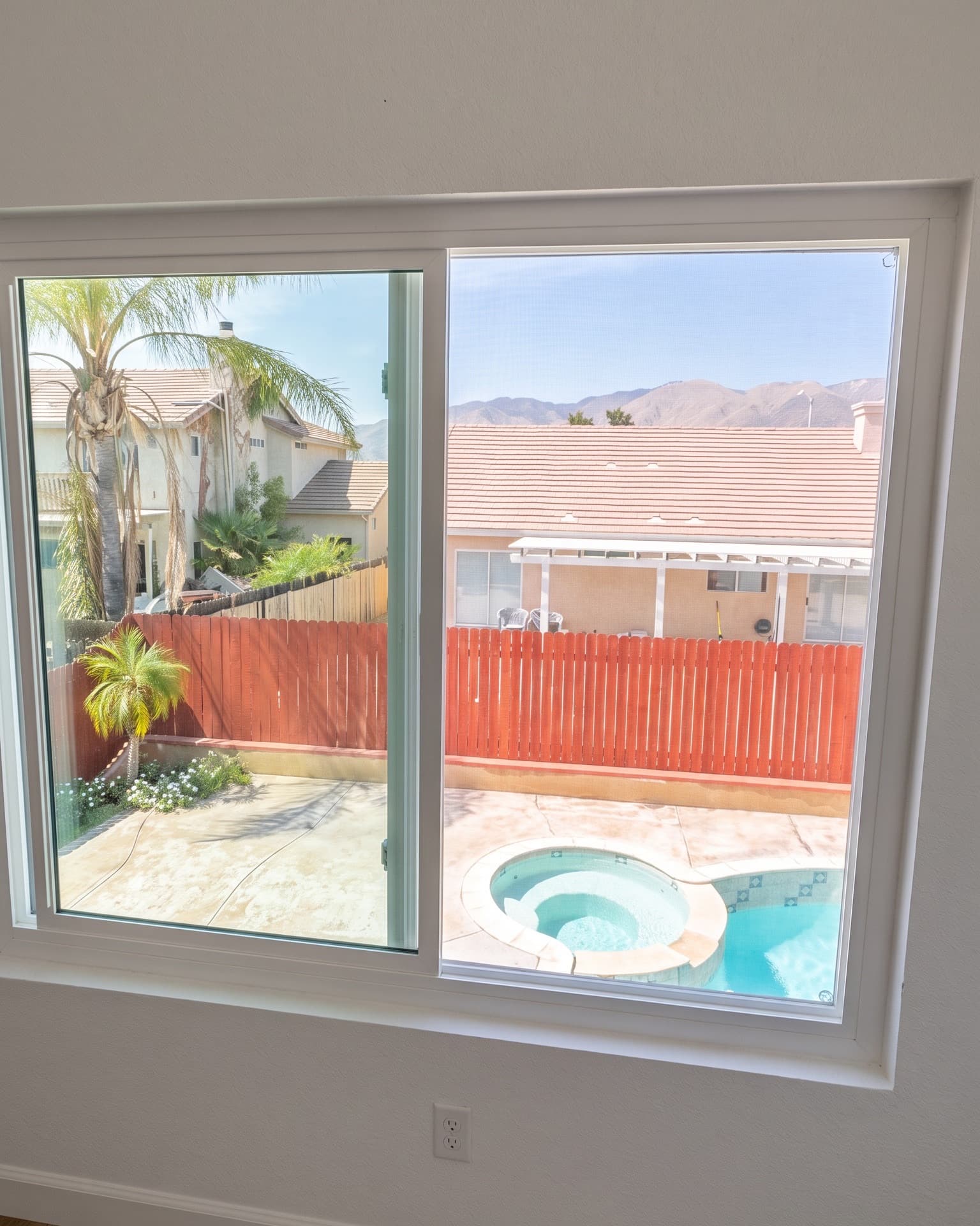 White sliding window looking out over a backyard pool and the mountains