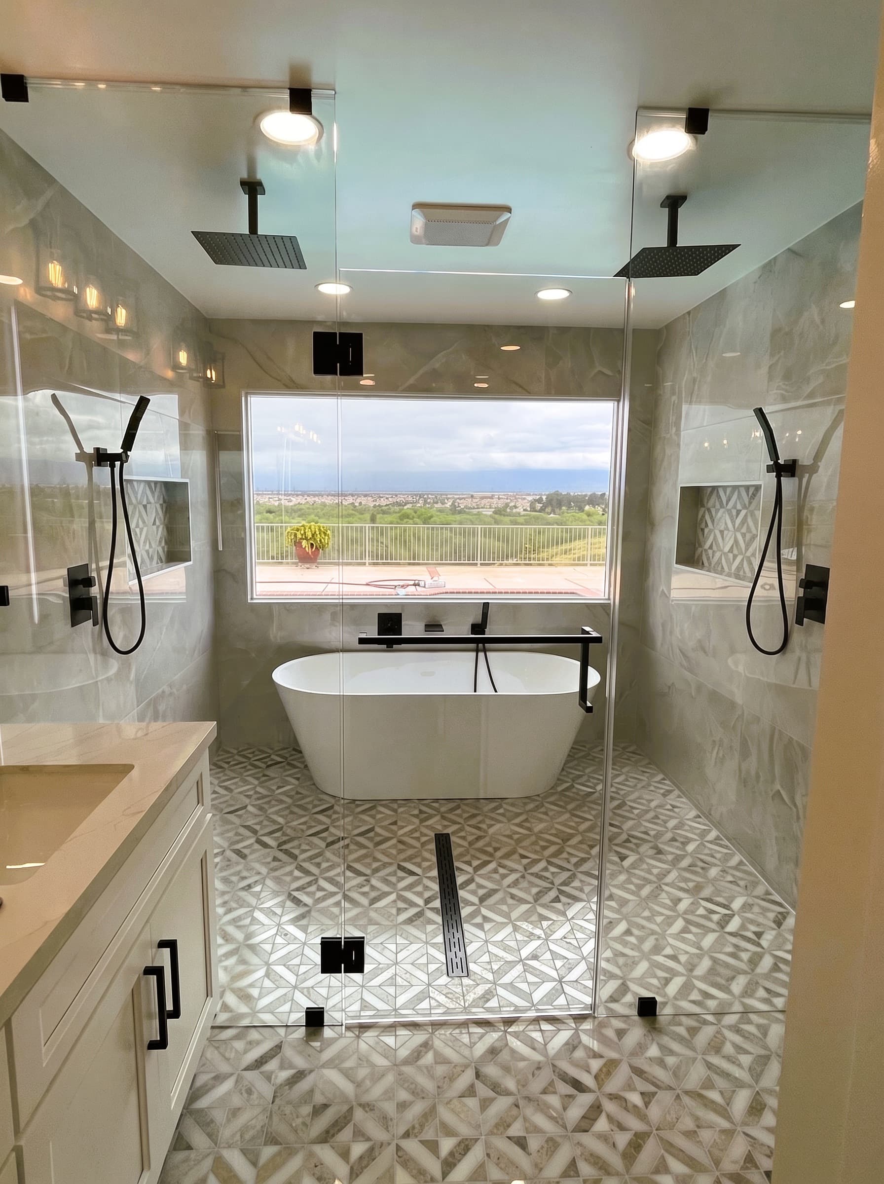 Frameless glass shower enclosure around a freestanding tub with a valley view